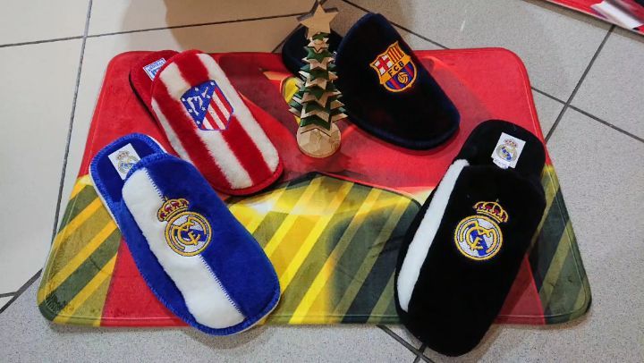 Pantuflas de equipos de fútbol español, incluyendo Real Madrid, FC Barcelona y Atlético de Madrid, sobre un tapete colorido con un árbol decorativo en el centro.
